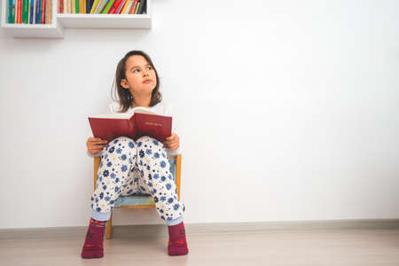 Happy smart schoolgirl reading Bible in next to library at home.の写真素材