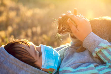 Little girl with mask playing with her cat during the pandemicの写真素材