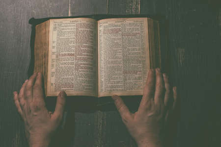 Prayer, man hands over an old open book Holy Bible, wooden desk background.の写真素材