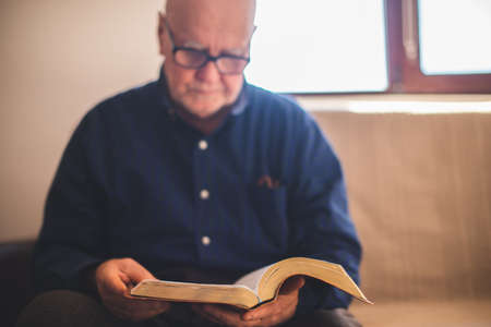 Elderly man sitting on couch and reading Bibleの写真素材