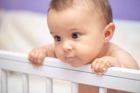 Infant child baby girl in white wooden bed looking curious.の写真素材