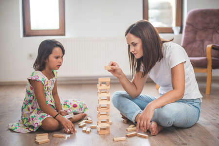 Young mother with her little daughter play game in wood blockの写真素材