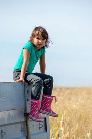 the portrait of a little girl sitting on the truck after she went to work on the farmの写真素材
