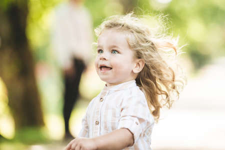 Cute little boy with curly blonde hair playing in parkの写真素材