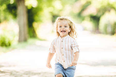 Cute little boy with curly blonde hair playing in parkの写真素材