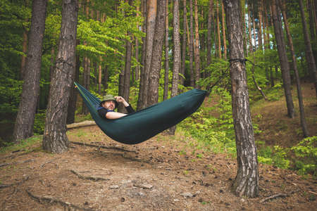 Man standing in a hammock on the edge of a forest admiring the landscapeの写真素材
