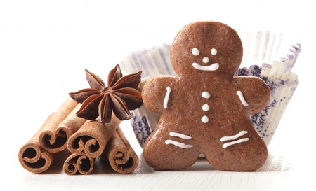 Close-up of gingerbread man, vanilla beans, anise stars, cinnamon sticks in paper cupcakes on white...