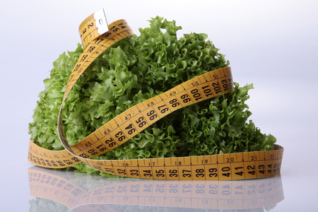Fresh salad lettuce and measuring tape on reflective white backgroundの写真素材