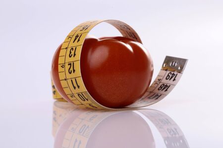 Ripe tomato and measuring tape on light reflective backgroundの写真素材