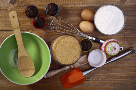 Ingredients and appliances for makeing cupcakes such as brown cane sugar flour and eggs on the wooden table, horizontal pictureの写真素材