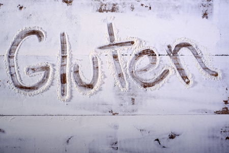 Wooden table top with gluten word text on flour background, horizontal pictureの写真素材