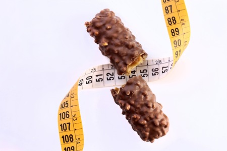 Appetizing chocolate bar broken in half with a measuring tape as a symbol of diet on white background, horizontal photoの写真素材
