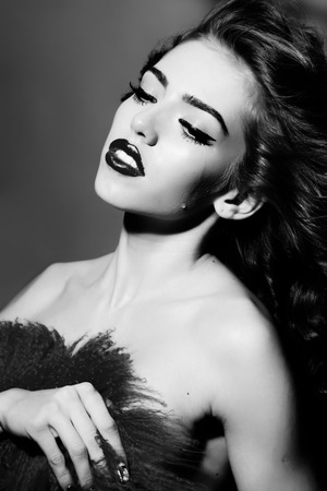 Portrait of beautiful young sophisticated naked girl with bright make up crying holding fur cloth standing on studio wall background black and white, vertical pictureの写真素材