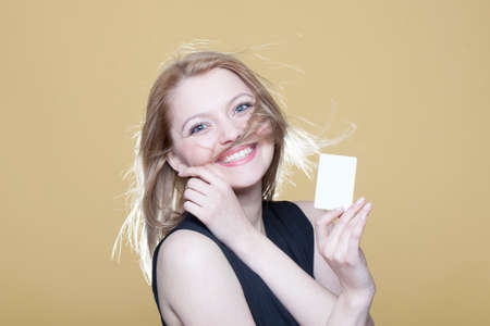 Happy young blonde girl with blank business card on beige backgroundの写真素材