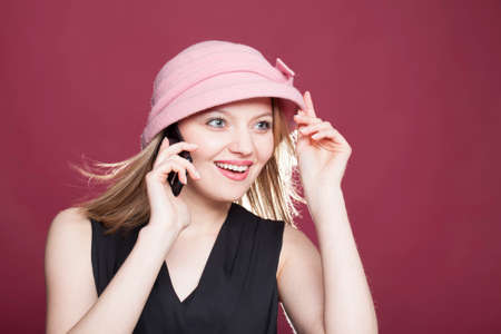 beautiful blonde woman in a hat with phone on red backgroundの写真素材
