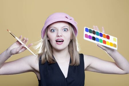 Surprised woman with paint and brush on beige backgroundの写真素材