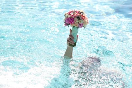 Male in swimming pool with blue water holding beautiful fresh wedding bunch of pink lilac purple white and violet chrysanthemum rose and peony flowers in hand copyspace, horizontal pictureの写真素材