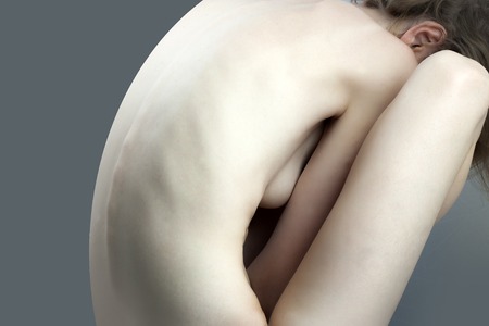 Beautiful slender naked female body perfect shape sitting with back view on grey background, horizontal pictureの写真素材