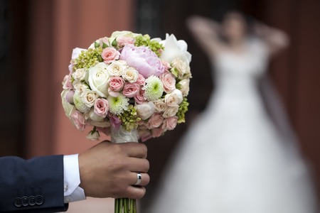 Groom holding beautiful fresh wedding bunch of pink lilac purple white and violet chrysanthemum rose and peony flowers in hand closeup on blur bride background, horizontal pictureの写真素材