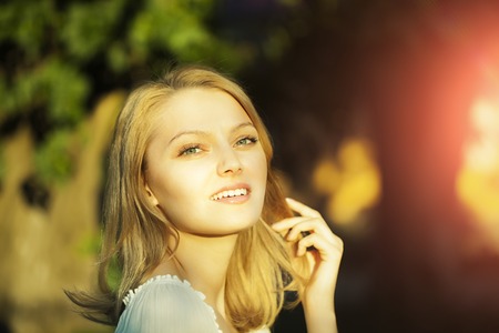 Portrait of smiling lively pretty young woman with blonde hair standing outdoor in sunset on natural background, horizontal pictureの写真素材