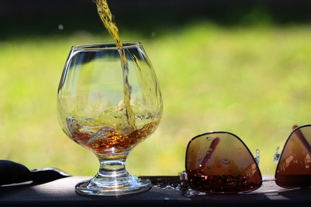 Amber alcoholic beverage poured in bocal stnading on table near sunglasses on natural background, horizontal pictureの写真素材