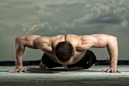 Handsome sexual muscular undressed man bodybuilder training on blue sky background, horizontal pictureの写真素材