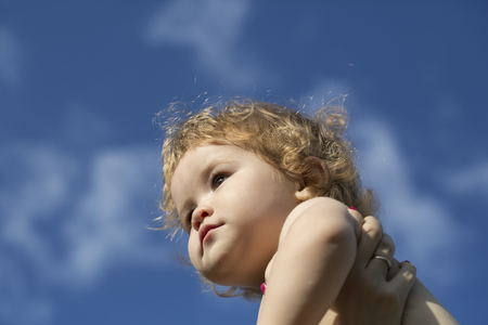 Little beautiful playful baby boy with blonde curly hair sunny day outdoor on blue sky background, horizontal pictureの写真素材