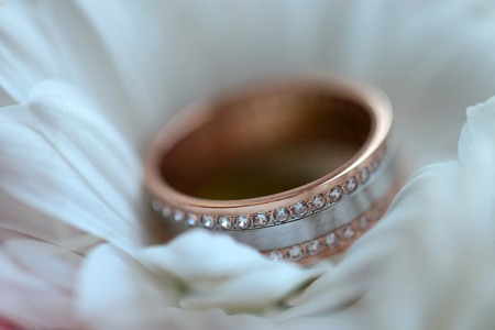 One golden wedding ring with diamonds on white fresh flower closeup, horizontal picture