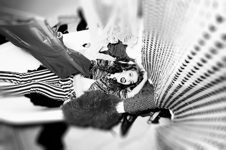 Striking emotional young girl with curly hair lying in bathtub amid clothes on wall background black...