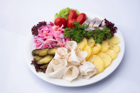Restaurant food of variety diner platter of marinated cucumbers tomatoes sauerkraut lard herring and rings boiled potatoes decorated with lettuce and parsley isolated on white, horizontal pictureの写真素材