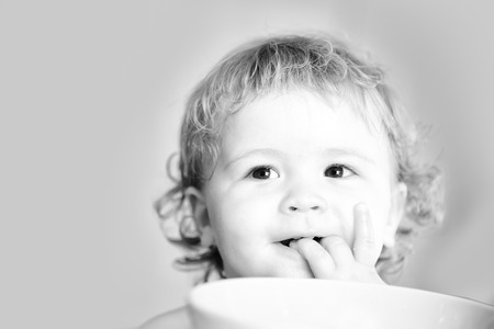 Portrait of sweet little smiling baby boy with curly hair and round cheecks lick fingers black and...