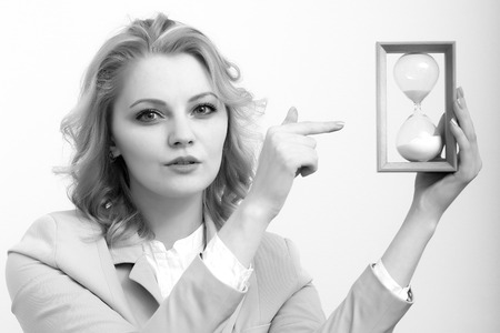 Portrait of serious beautiful business woman with curly hair in jacket showing on hour glass clock...