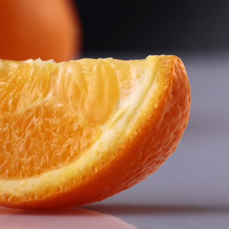 Closeup of one lobule of fresh juicy ripe appetizing orange in front lying on grey reflecting surface in studio isolated on black background, square pictureの写真素材