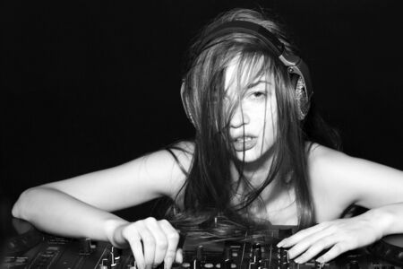 Portrait of young art cute sexy disk jockey girl in headphones with naked shoulders and long hair near professional musical mixer console black and white, horizontal pictureの写真素材