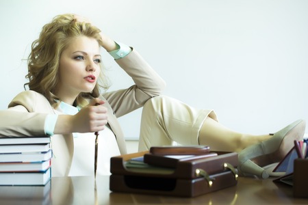 Pretty thoughtful sensual business woman sitting at table with many office appliances holding knife for cutting paper looking forward on white background copyspace, horizontal pictureの写真素材