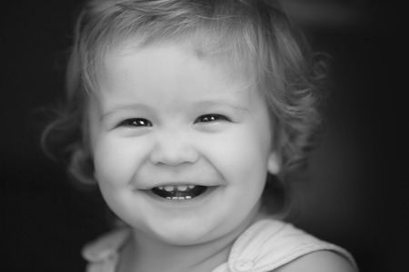 Portrait of little laughing pretty male kid with curly hair looking forward outdoor on dark...