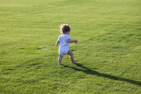 Happy runaway curly barefoot little boy on summer green grass meadow sunny day outdoor, horizontal photoの写真素材