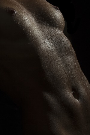 Closeup of naked sexual wet female body of young girl in water drops with beautiful breast nipples and flat belly on black background, vertical pictureの写真素材