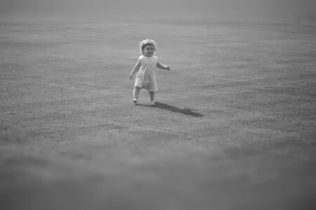 Small cute smiling baby boy with curly hair in light summer clothes maing step on field with fresh grass sunny day outdoor black and white copyspace, horizontal pictureの写真素材