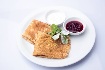Appetizing fried pancakes folded square with berry jam and sour cream decorated with mint leaves sprinkled with powdered sugar isolated on white, horizontal pictureの写真素材