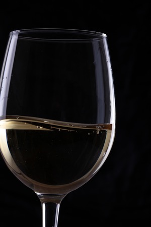 Closeup of one transparent clear elegant glass bocal with white grape rough wine with bubbles in studio isolater on black background, vertical pictureの写真素材