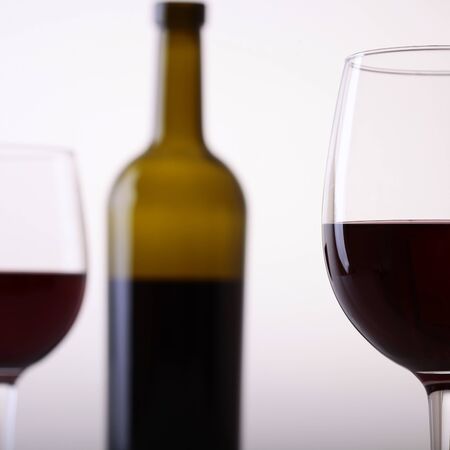 One blur green bottle and two glass goblets with red grape wine standing in studio isolated on white backgroung, square pictureの写真素材