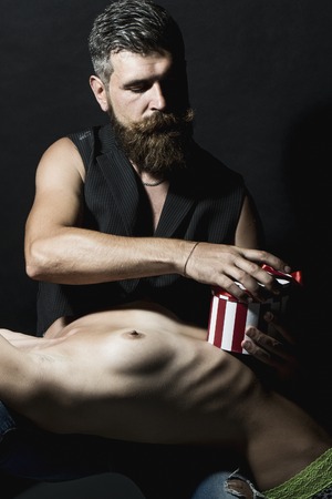 Sexy young people of undressed girl in green panties lying on  unshaven man with beard and moustache smoking cigarette in waistcoat on black background, vertical pictureの写真素材