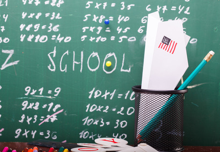 Colorful pencils of red yellow orange violet purple pink green and blue stationary cup ruler fan english alphabet and paper plane with back to school text written with white chalk blackboard on mathの写真素材