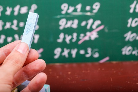 Human hand holding one blue chalk and heap of colorful pieces  pastel pink violet green blue yellow...