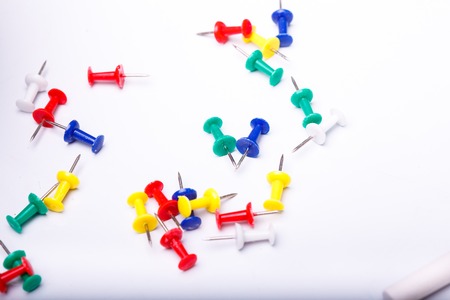 Many colorful drawing-pins of red yellow green blue lying on white school desk background copyspace,...
