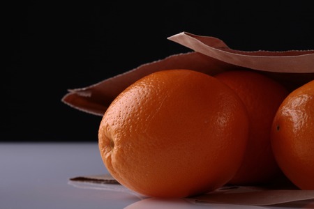 Closeup of fresh juisy bright tasty whole orange in brown paper packet with heap of citrus fruit...
