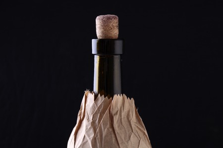 Closeup of one glass green wine corked bottle with alcohol beverage with cork in brown paper packet isolated on black studio background copyspace, horizontal pictureの写真素材