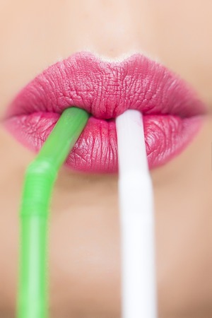 Closeup of sexual closed female mouth of beautiful young woman with bright pink lips drinking some beverage with two drinking straws white and green colours, vertical pictureの写真素材