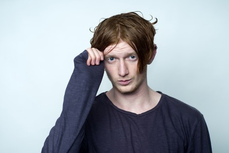 Portrait of sensual cute young boy model touching red hair with hands in grey jersey looking forward standing in studio on white , horizontal pictureの写真素材
